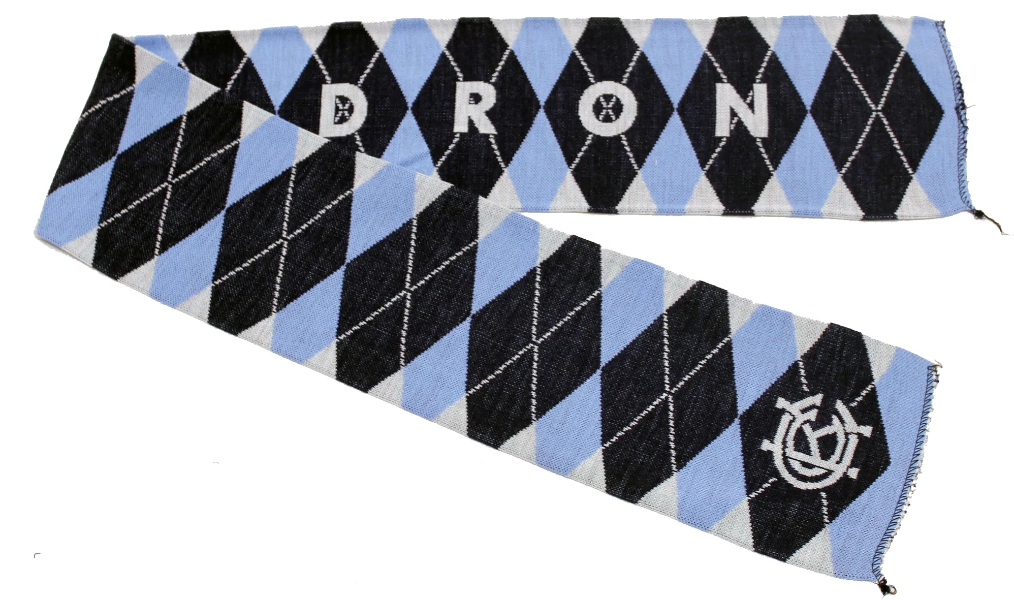 A scarf with a geometric argyle pattern in navy, blue, and white colors, with text that reads 'CAULDRON'. The KCC logo appears on the obverse ends.