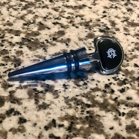 Bottle stopper with white KCC Logo laying on a granite countertop