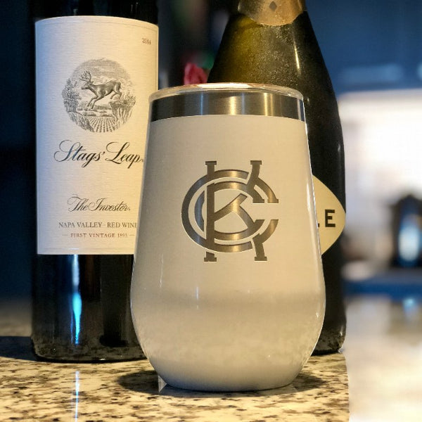 A white insulated wine cup and lid with a KCC logo printed on it, placed next to a wine bottle and a cork.