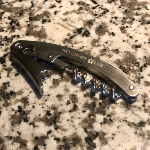 Corkscrew with 'No Other Club' branding on a marble surface